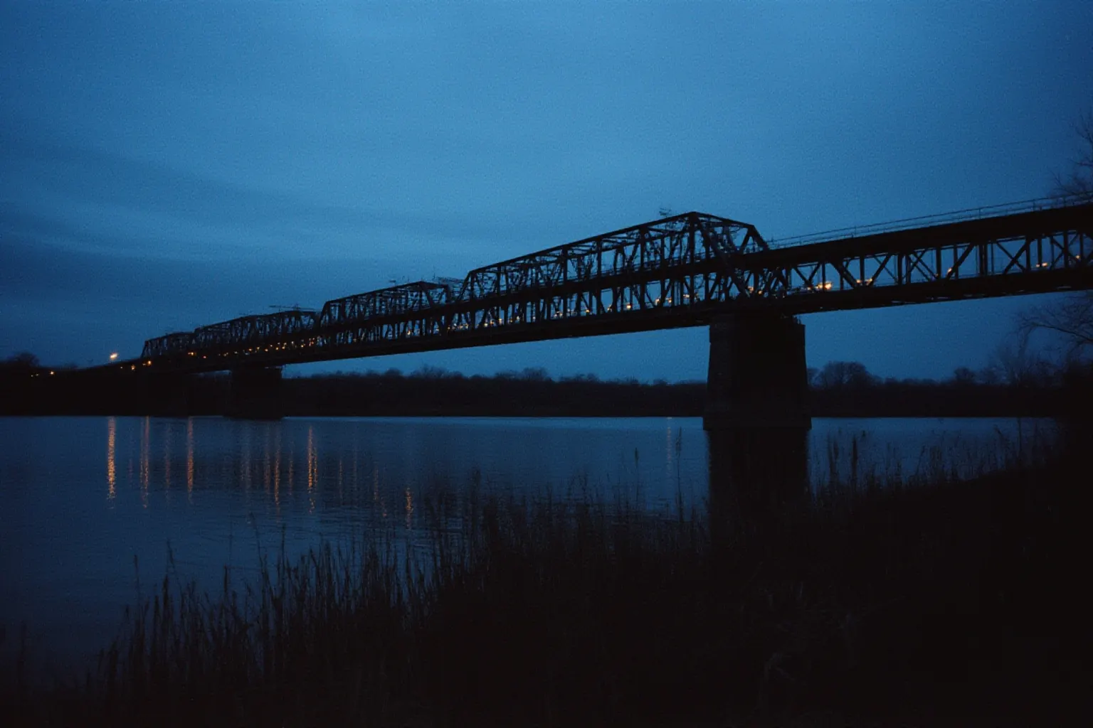 Steel truss bridge over a river at dusk with faint light trails