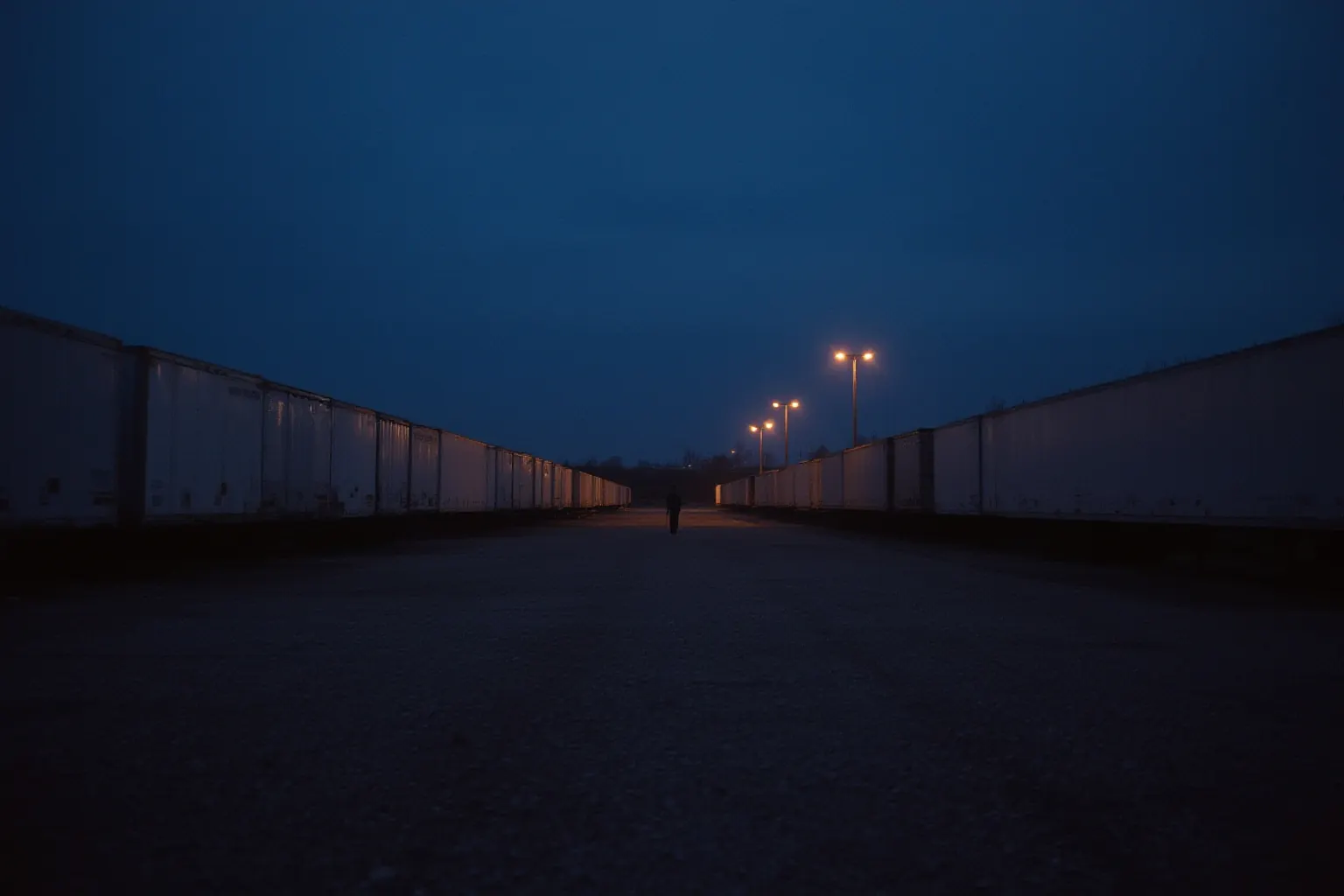 Distant worker silhouette among trailers in a freight yard at dusk