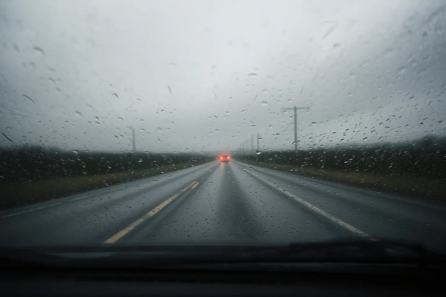Rain-beaded windscreen view of an empty two-lane road